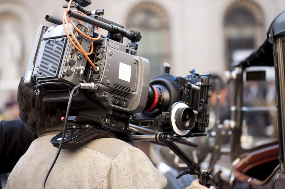 The cameraman is surrounded by directors, producers, grips, and other members of the film crew.