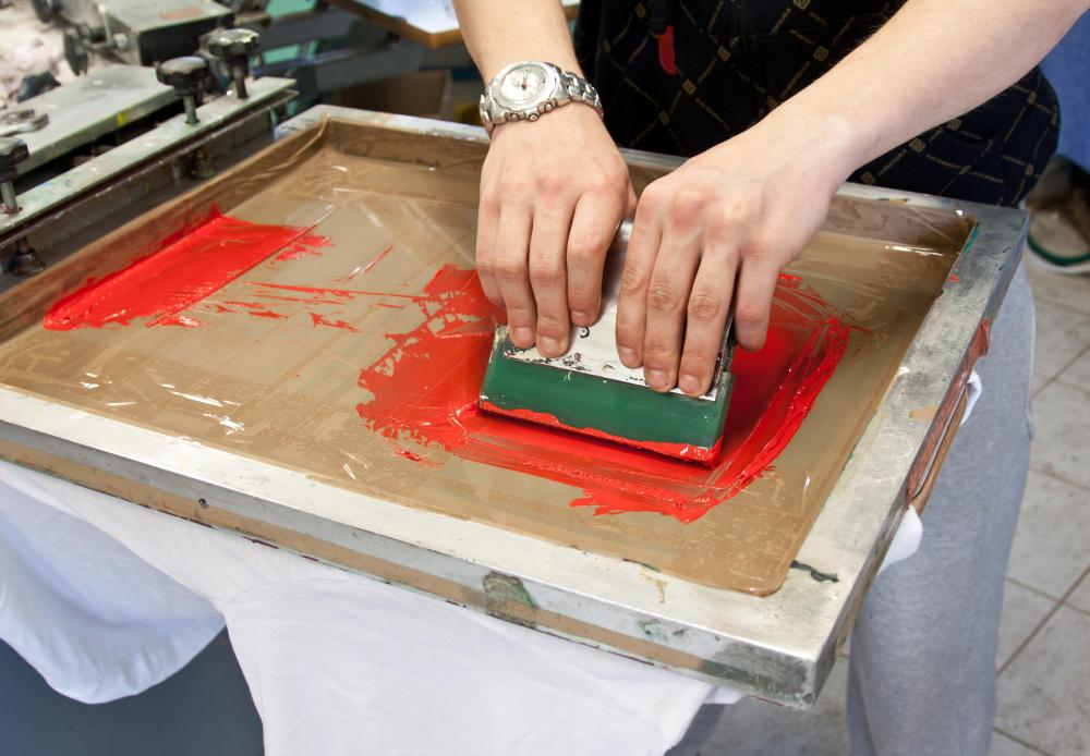 The operator uses a squeegee to press ink through to the material in screen printing.