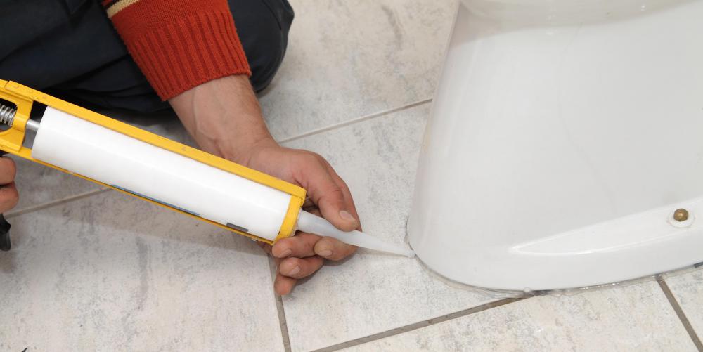 Sealing toilet on a bathroom floor with caulk.